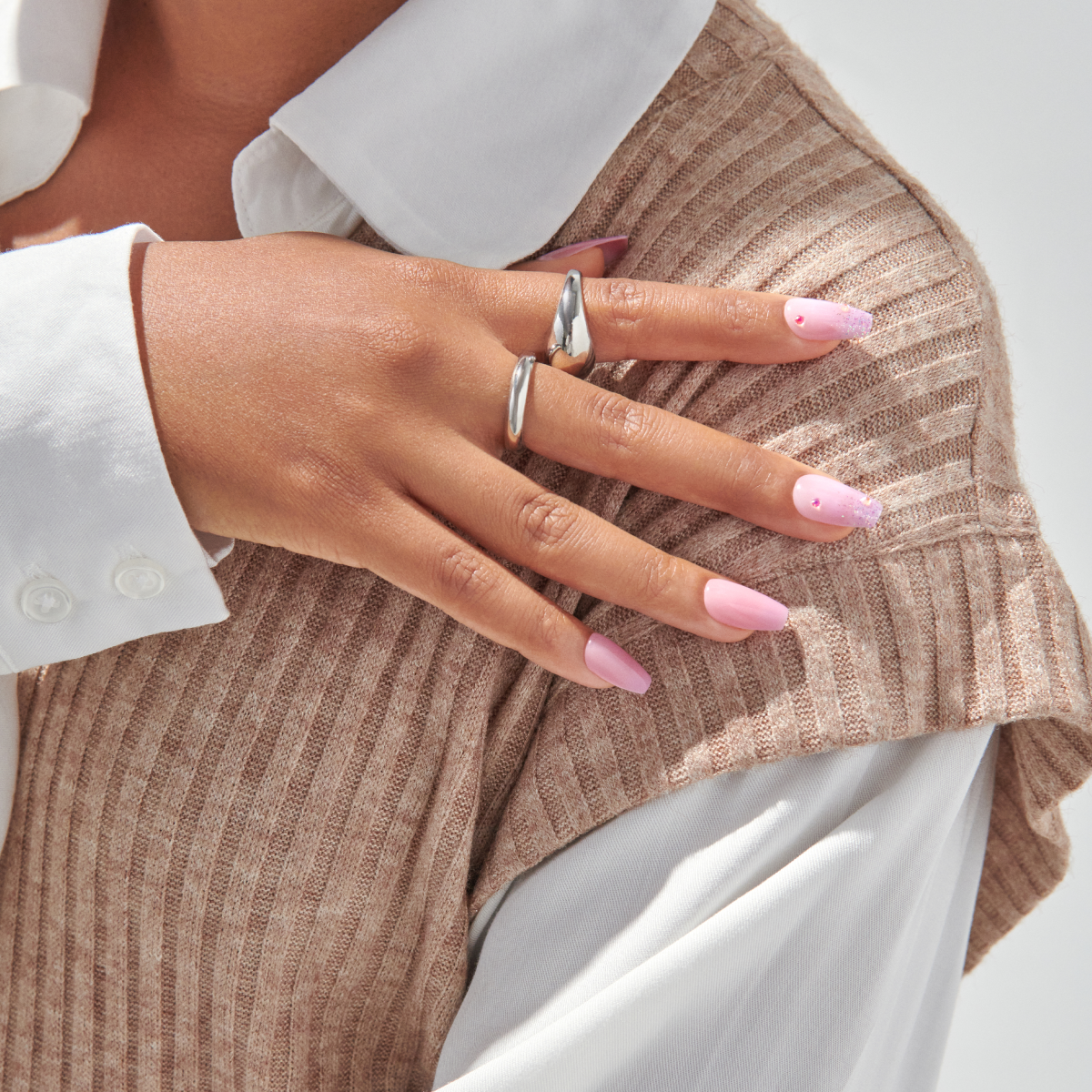 Woman wearing silver rings displaying pink ombre manicure and beige sweater