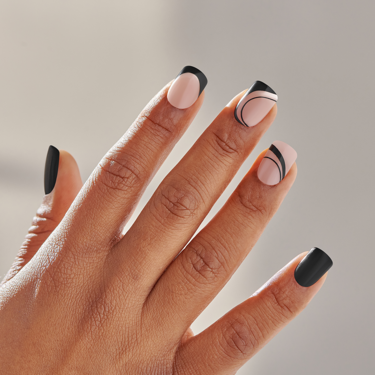 Hand displaying five nail designs with black tips and nude bases, featuring geometric line accents.