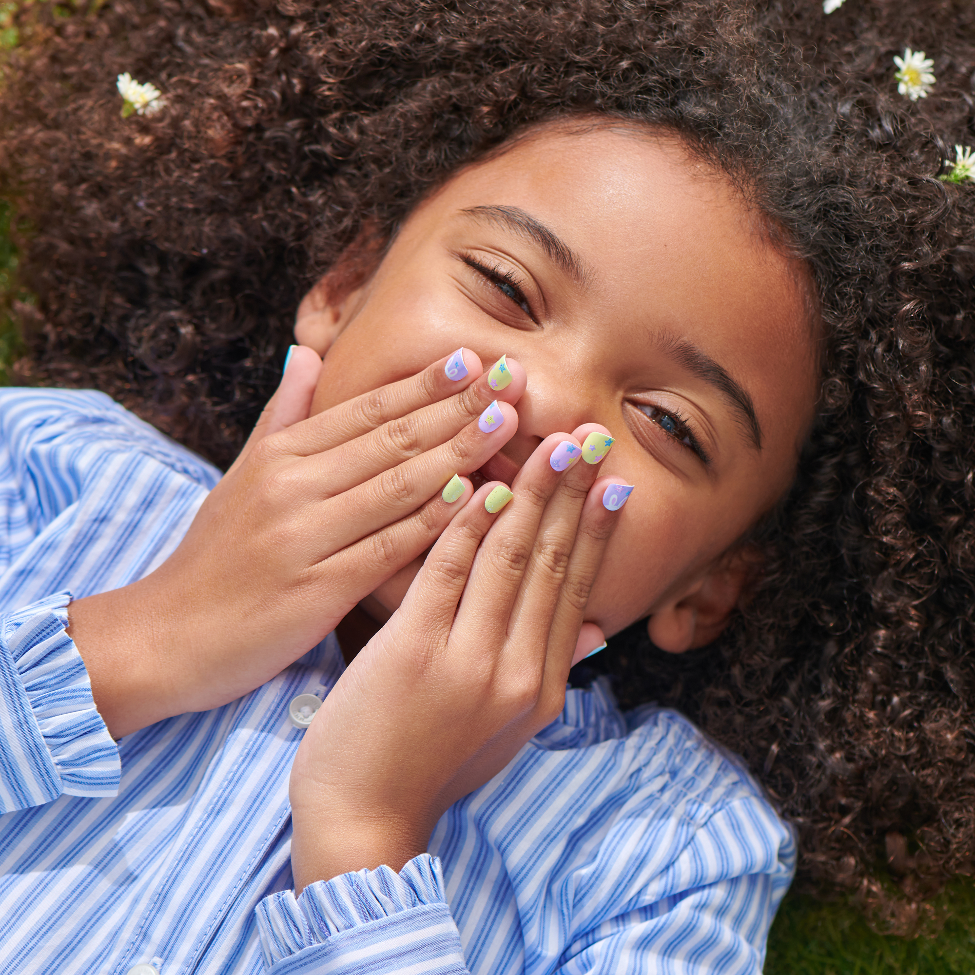 Young person with colorful pastel nail polish lying on ground outdoors