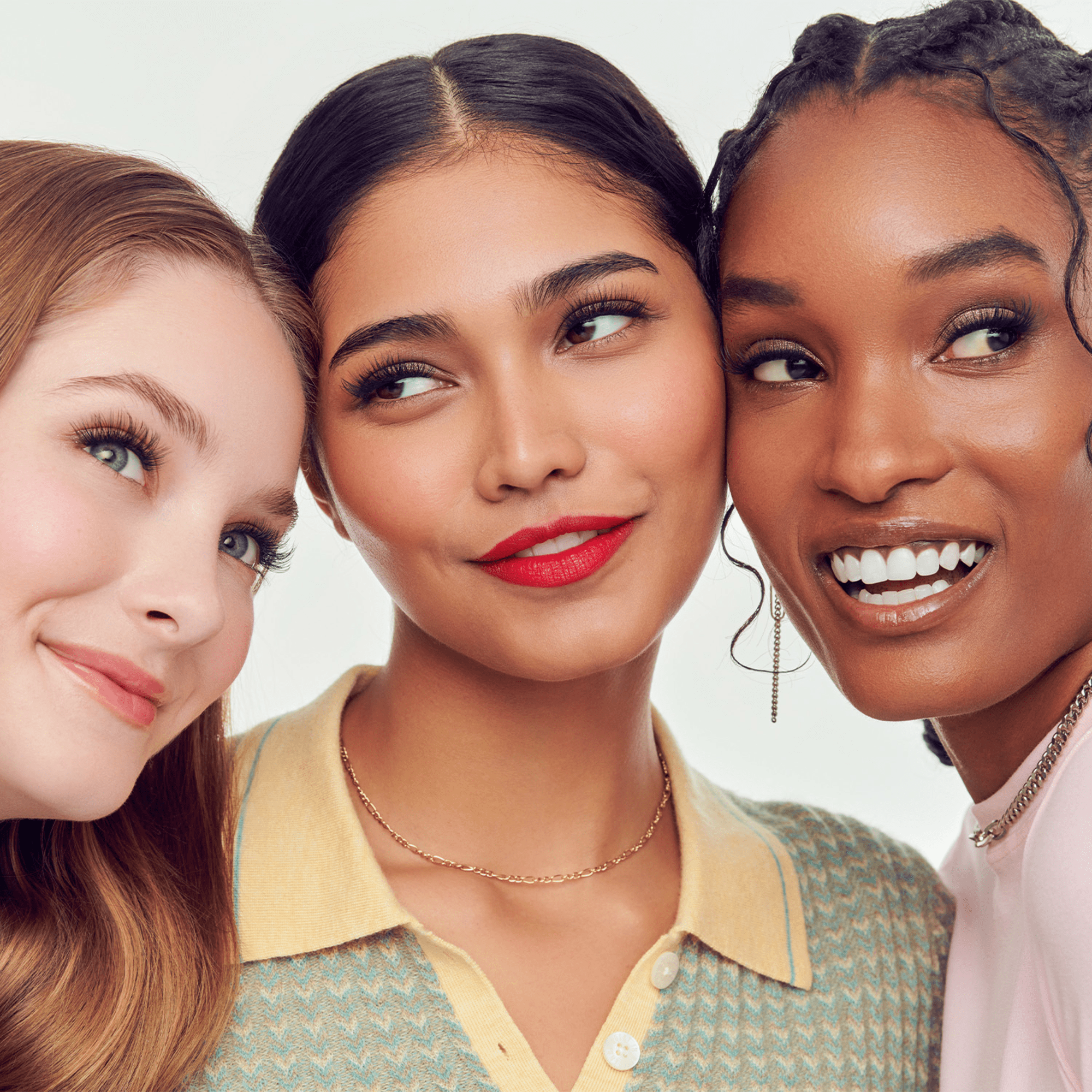 Three women with different skin tones and hairstyles posing together.