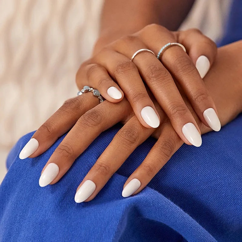 A woman wearing a blue dress with white nails press on nails. The nail shape is oval with a medium length nail.