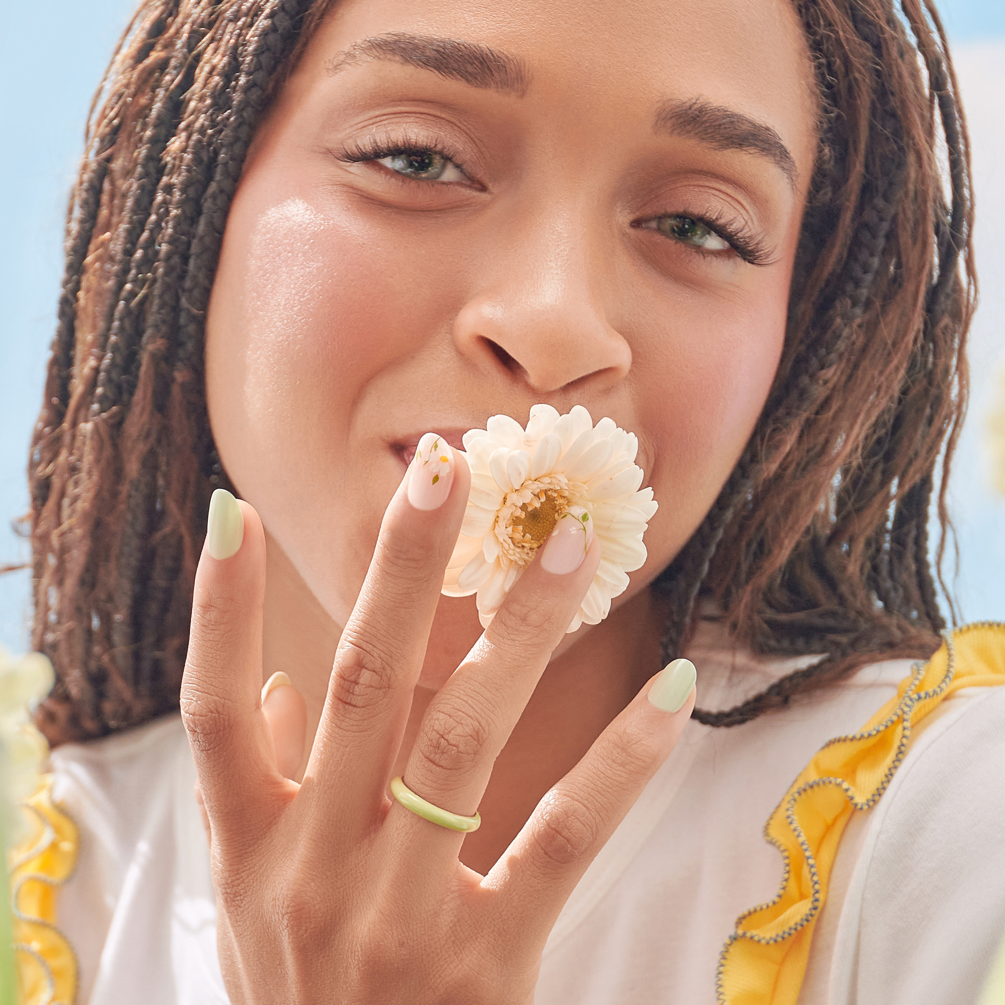 Woman with braids holding pale pink flower, wearing soft yellow nail polish and rings.