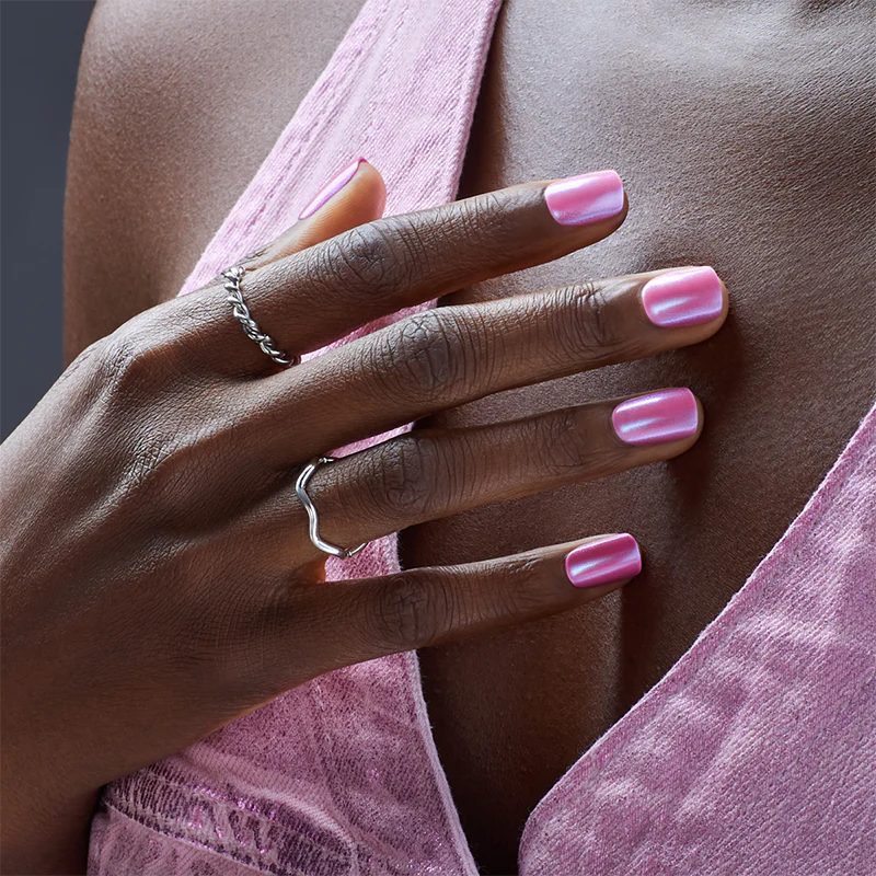 A hand modeling a short, square shaped manicure in a bubble gum pink, mirrored effect. Nails are press on from imPRESS. No glue needed for 7 days of wear.