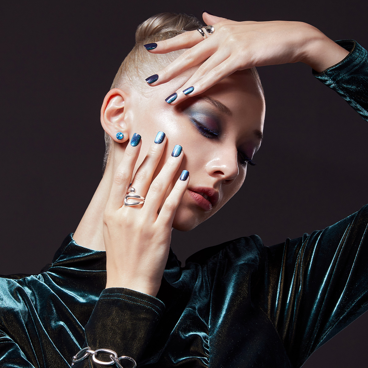 Woman posing with her hands against her face with a dark green, mirror effect press-on manicure from &
