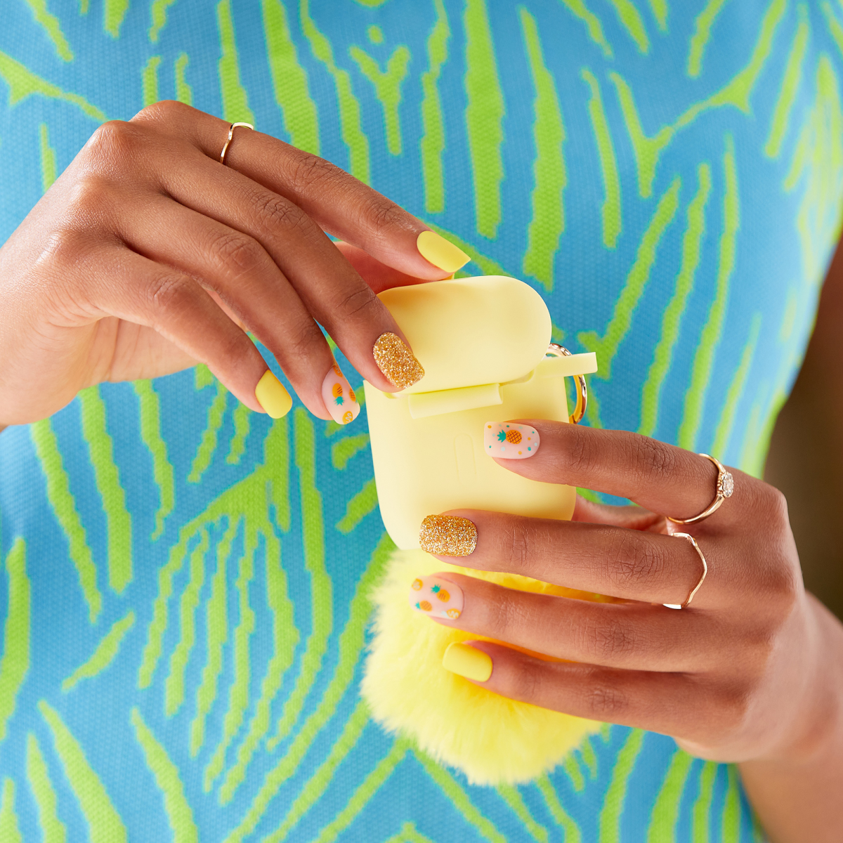 Person holding yellow skincare jar, displaying colorful nail art against blue and green striped background.