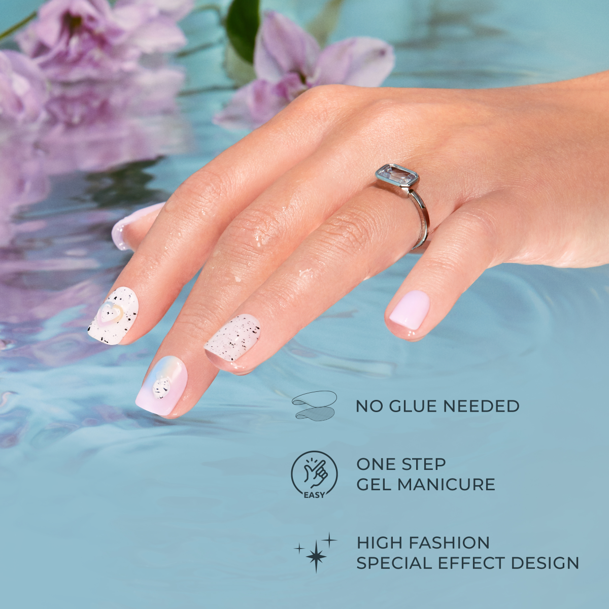 Hand wearing gel manicure with pink and white speckled nails and ring against blue background with flowers.