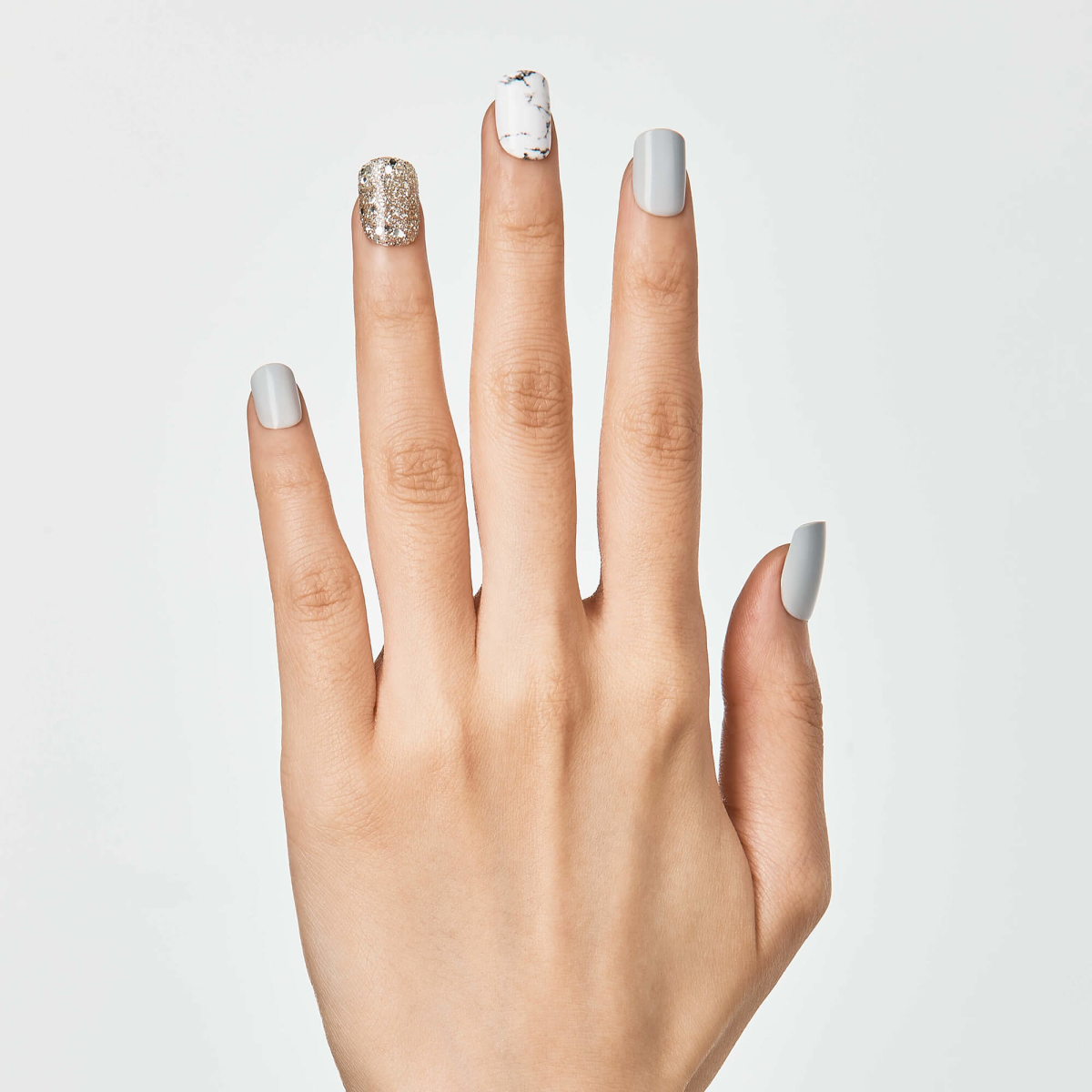 Hand displaying four nail polish designs: silver glitter, white marble, solid silver, and nude with silver accent.