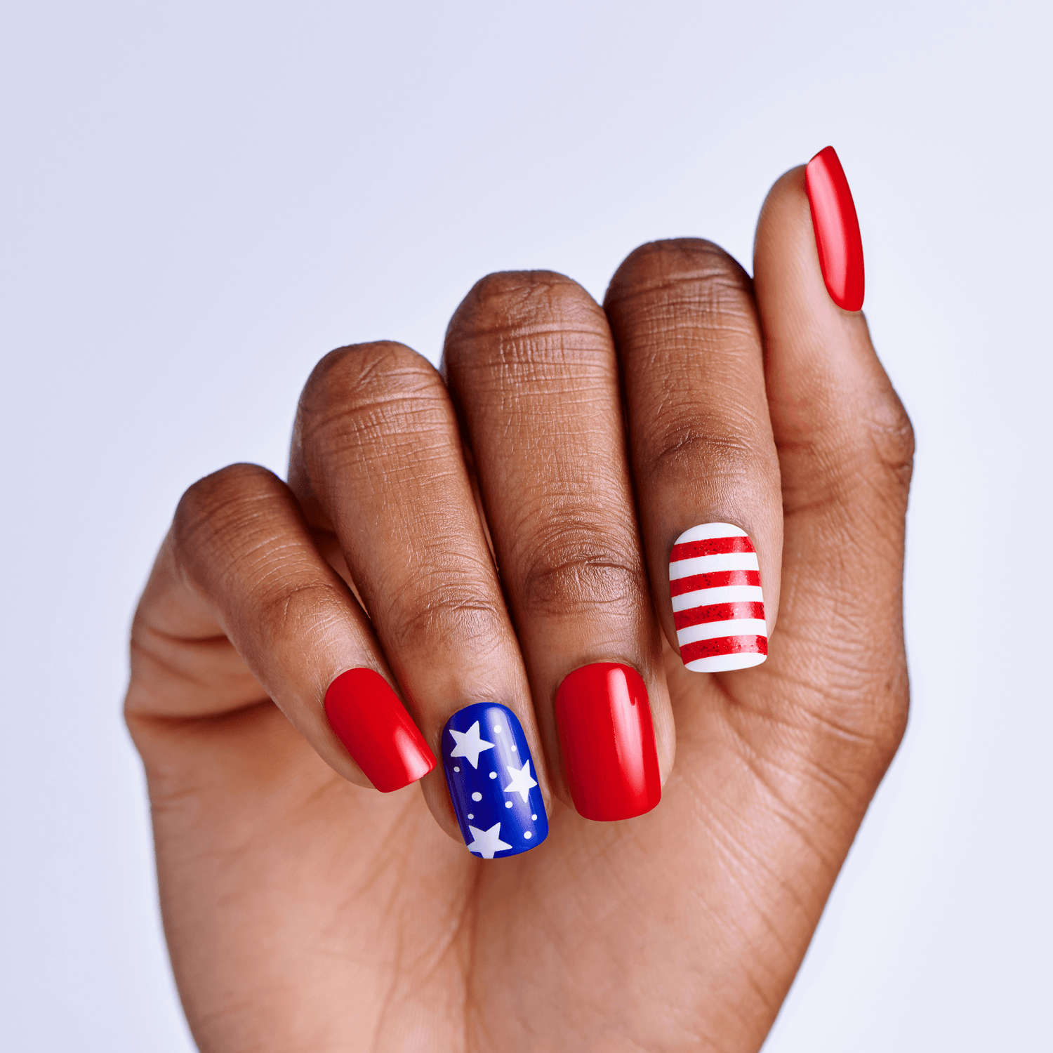 Hand with red, white, and blue nail polish on a light gray background