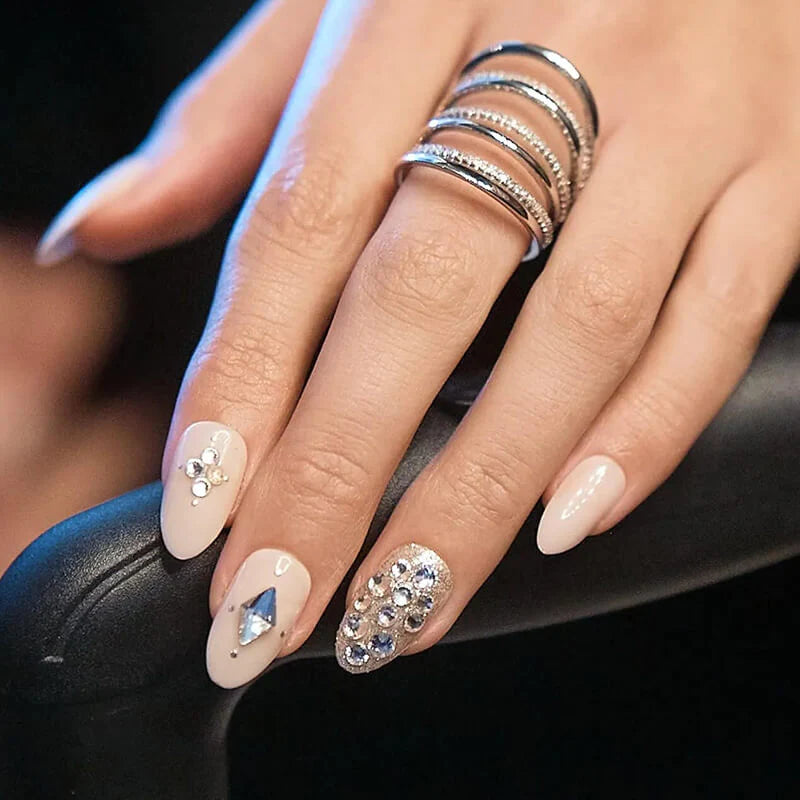 A hand modeling a medium, almond shaped manicure in nude color and 3D jewel designs. Nails are press on from imPRESS. No glue needed for 7 days of wear. 