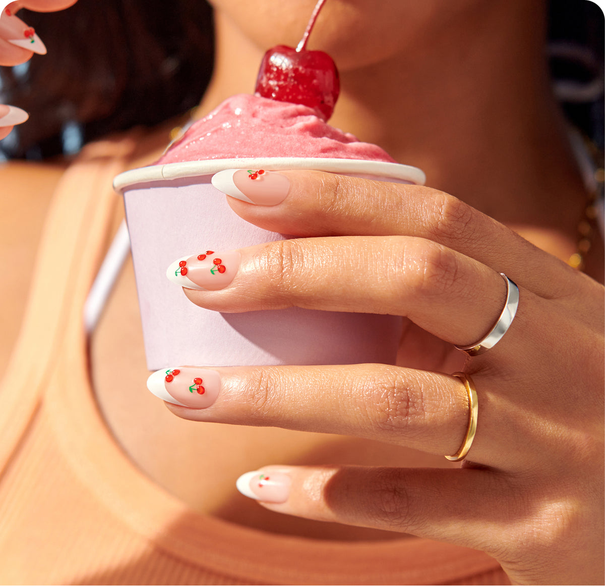 Woman's hand holding pink cup with cherry nail art design and manicure