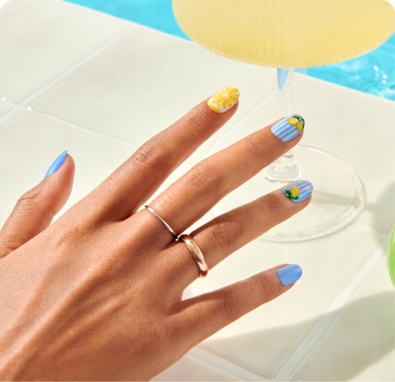 Summer-themed manicure with blue and yellow lemon nail designs on poolside setting.