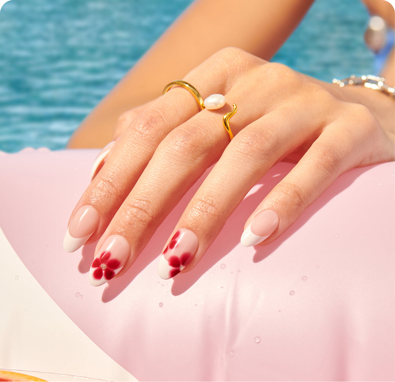 Manicured nails with red floral design and gold pearl ring by poolside