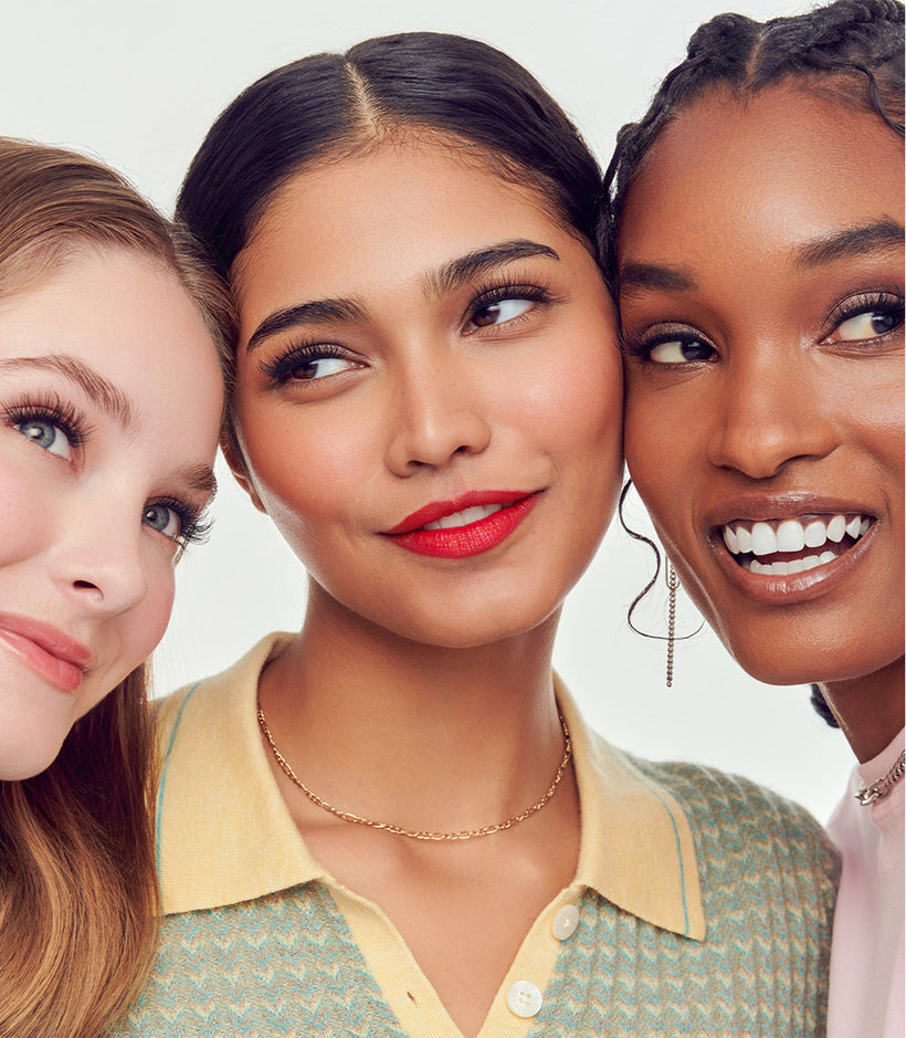 Three women of diverse ethnicities displaying false lashes and makeup styles against white background.
