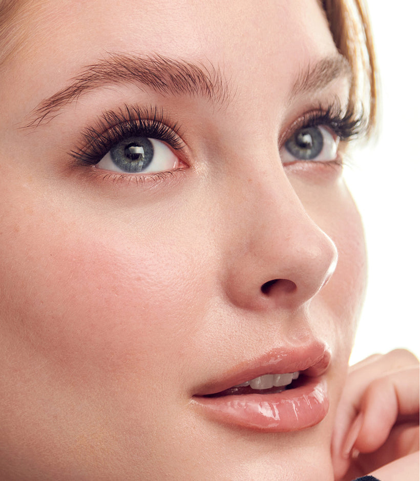 Woman wearing KISS Impress falsies, showcasing black mascara and natural makeup.