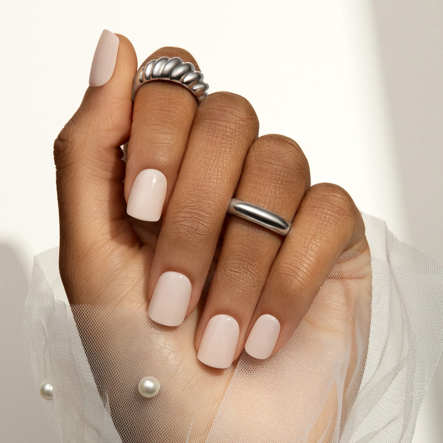Hand with light pink nail polish and silver rings on a neutral background
