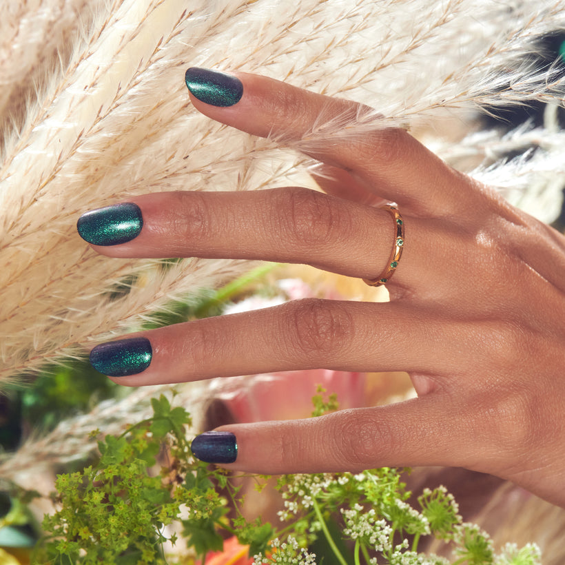 Hand with teal glitter nails and gold ring near white flowers and pampas grass