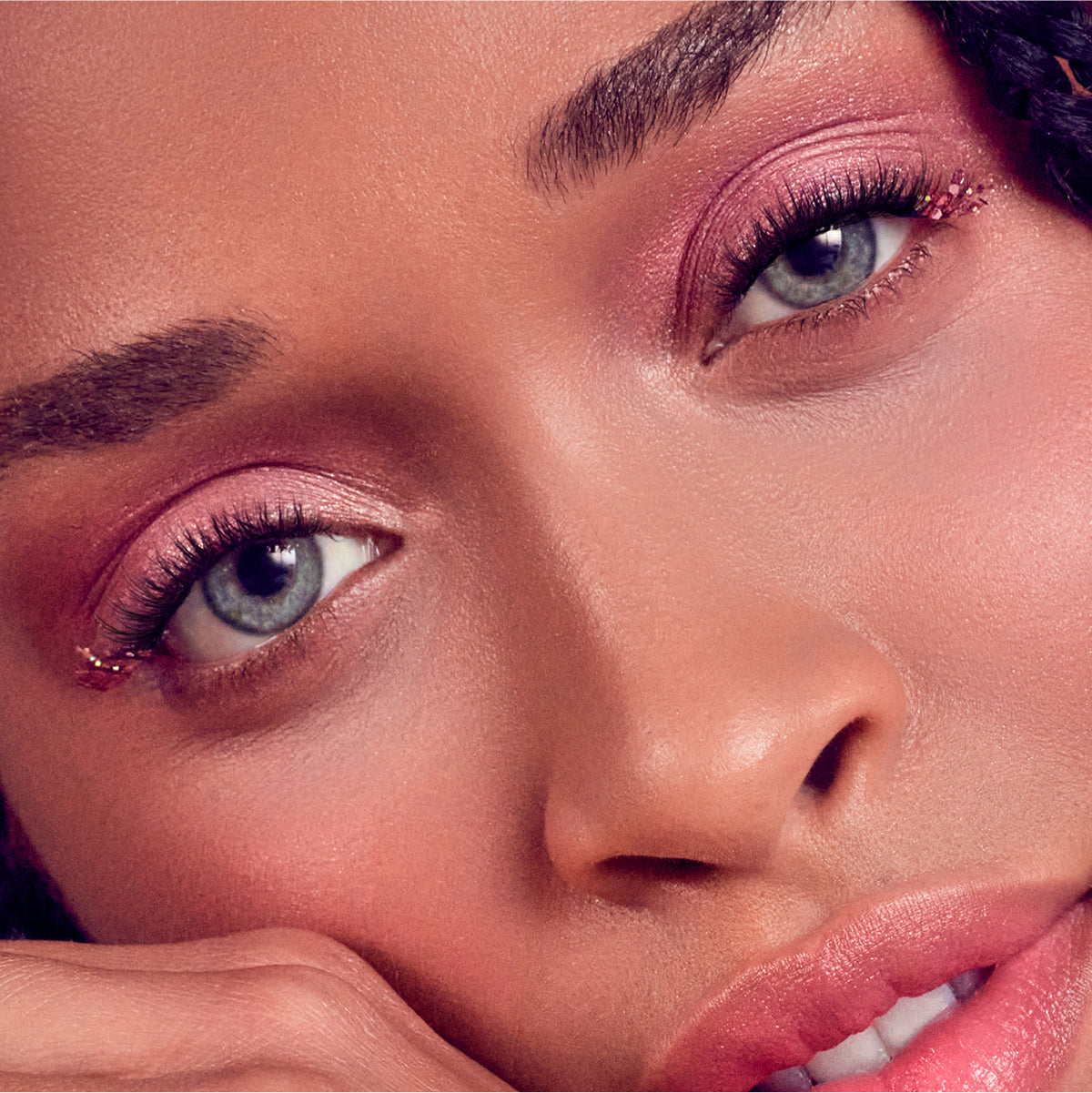 Close-up of face with pink eyeshadow, glitter eyeliner, and pink lipstick makeup look.