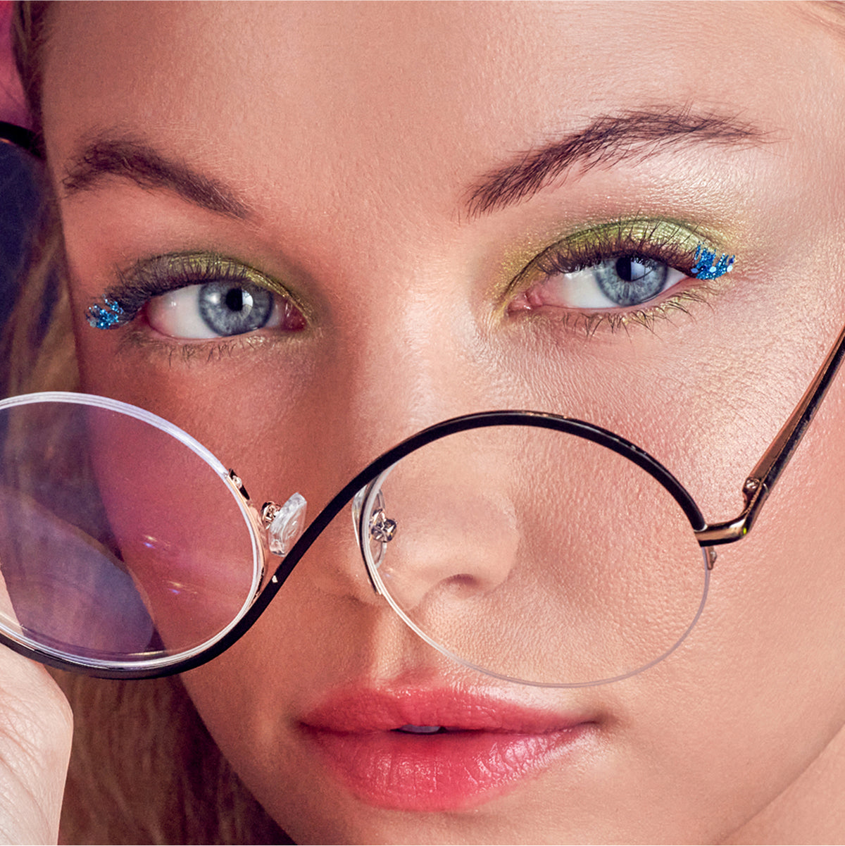 Close-up of person wearing round glasses with glittery blue eyeshadow and gold eyeliner.