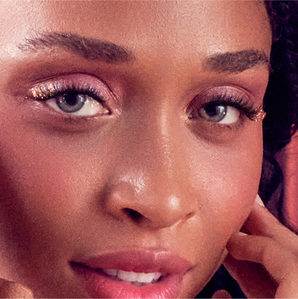 Close-up of model's face with gold eyeshadow, defined brows, and pink lipstick.