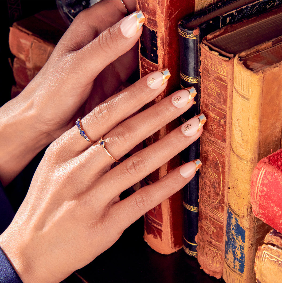 Elegant French manicure nails with gold accents near antique leather books