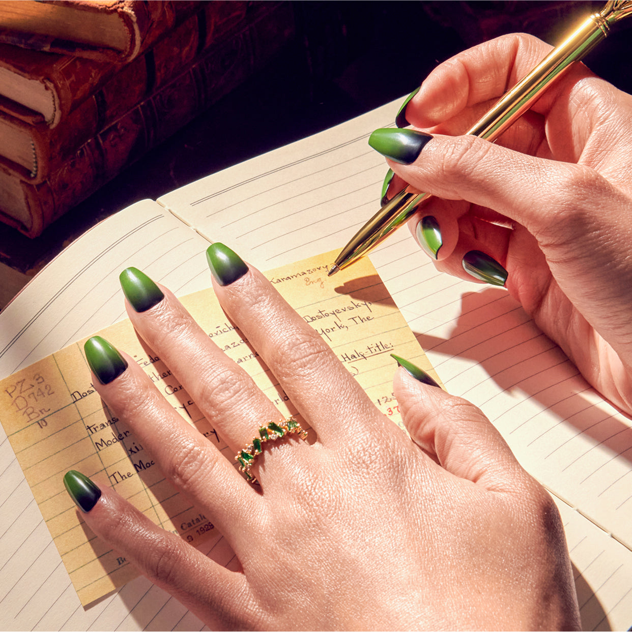 Woman writing in journal with green ombre nails and emerald ring.