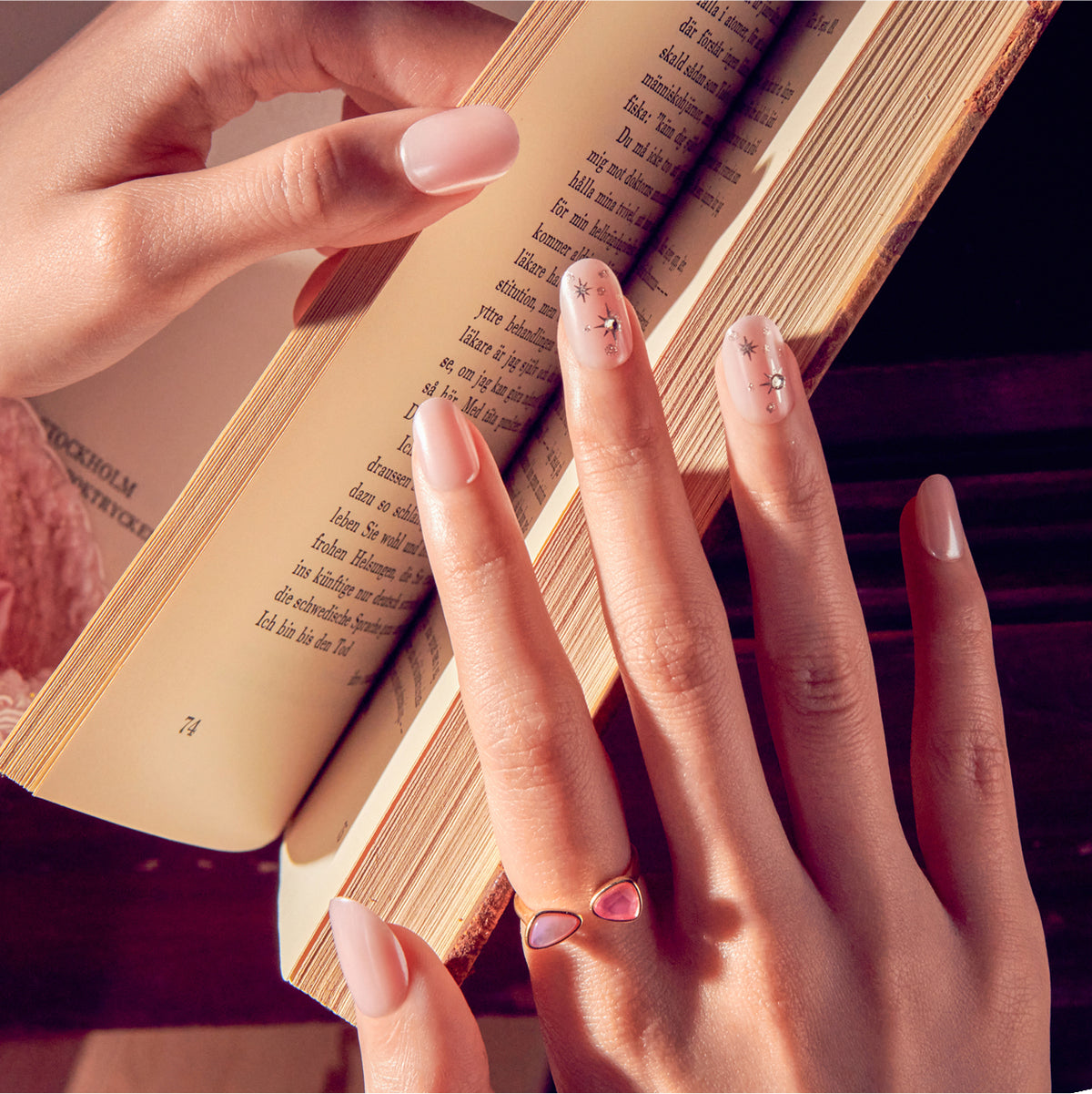 Woman's manicured hand holding open book with delicate nail art and rings.