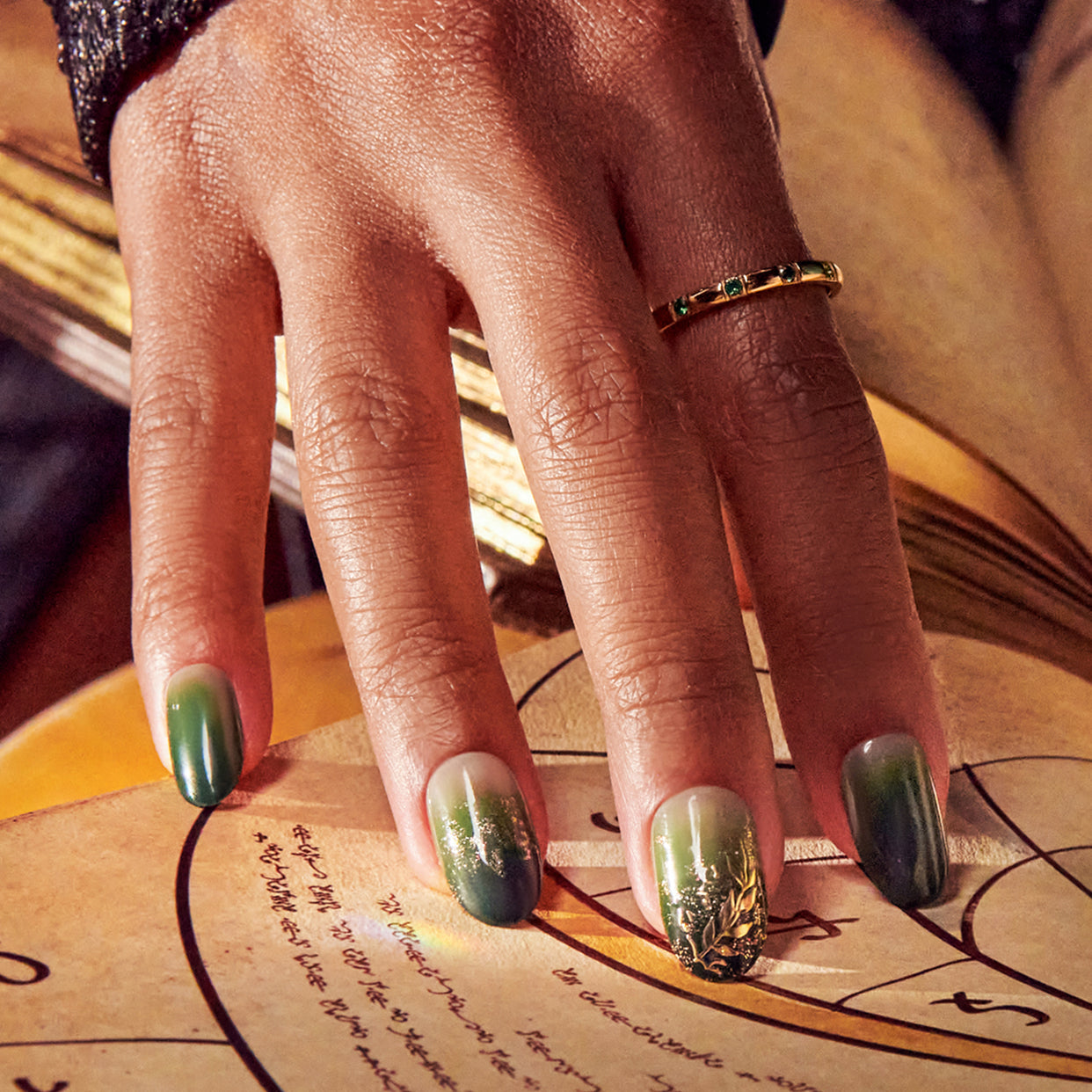 Manicured hand with green and gold nail art on written document, wearing gold ring.