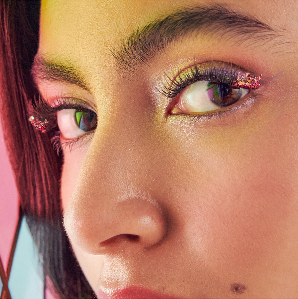 Close-up of eyes with bold glitter eyeshadow, winged eyeliner, and colorful iris reflections.