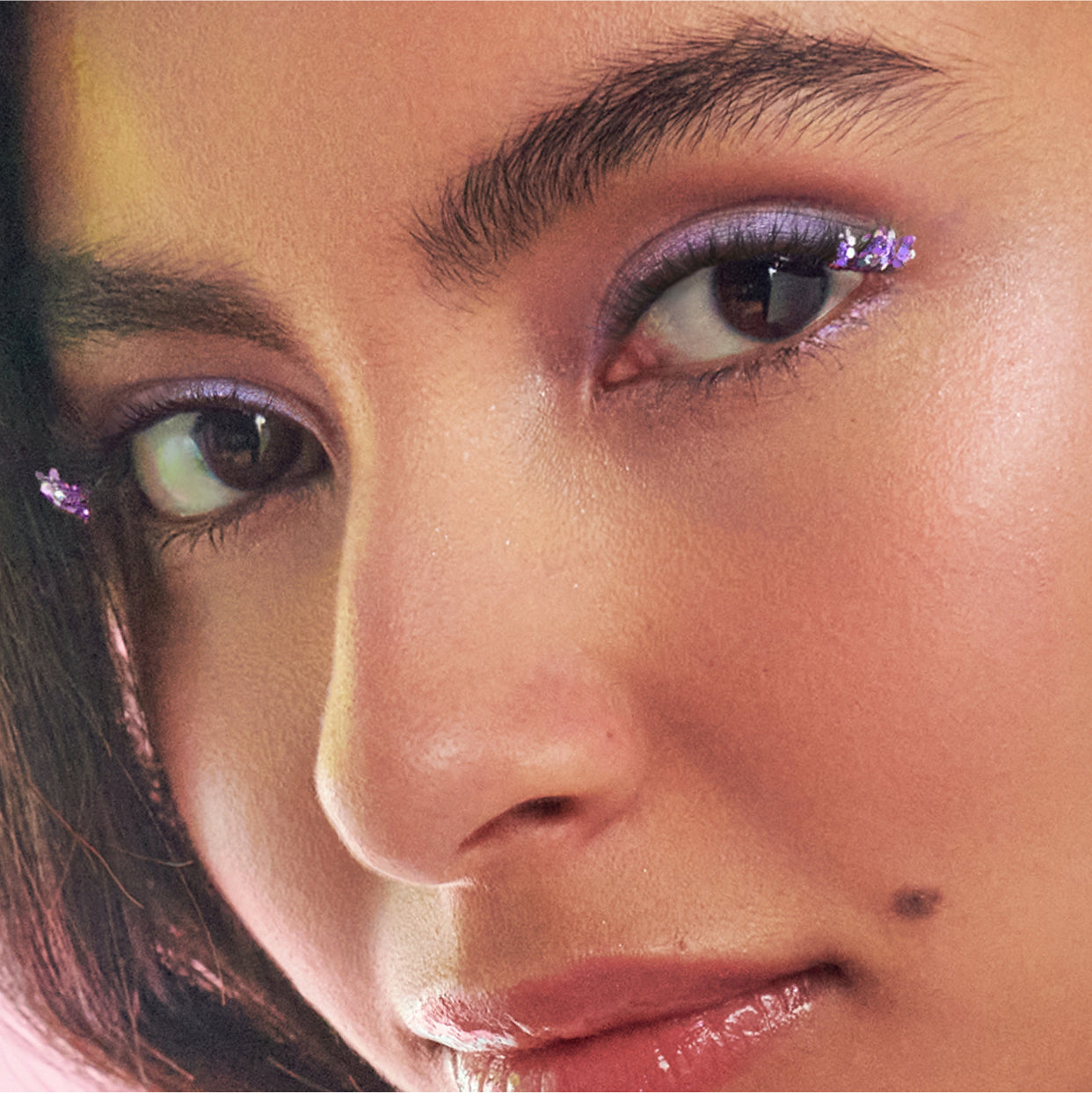 Close-up of face with purple glitter eye makeup and mauve lip gloss