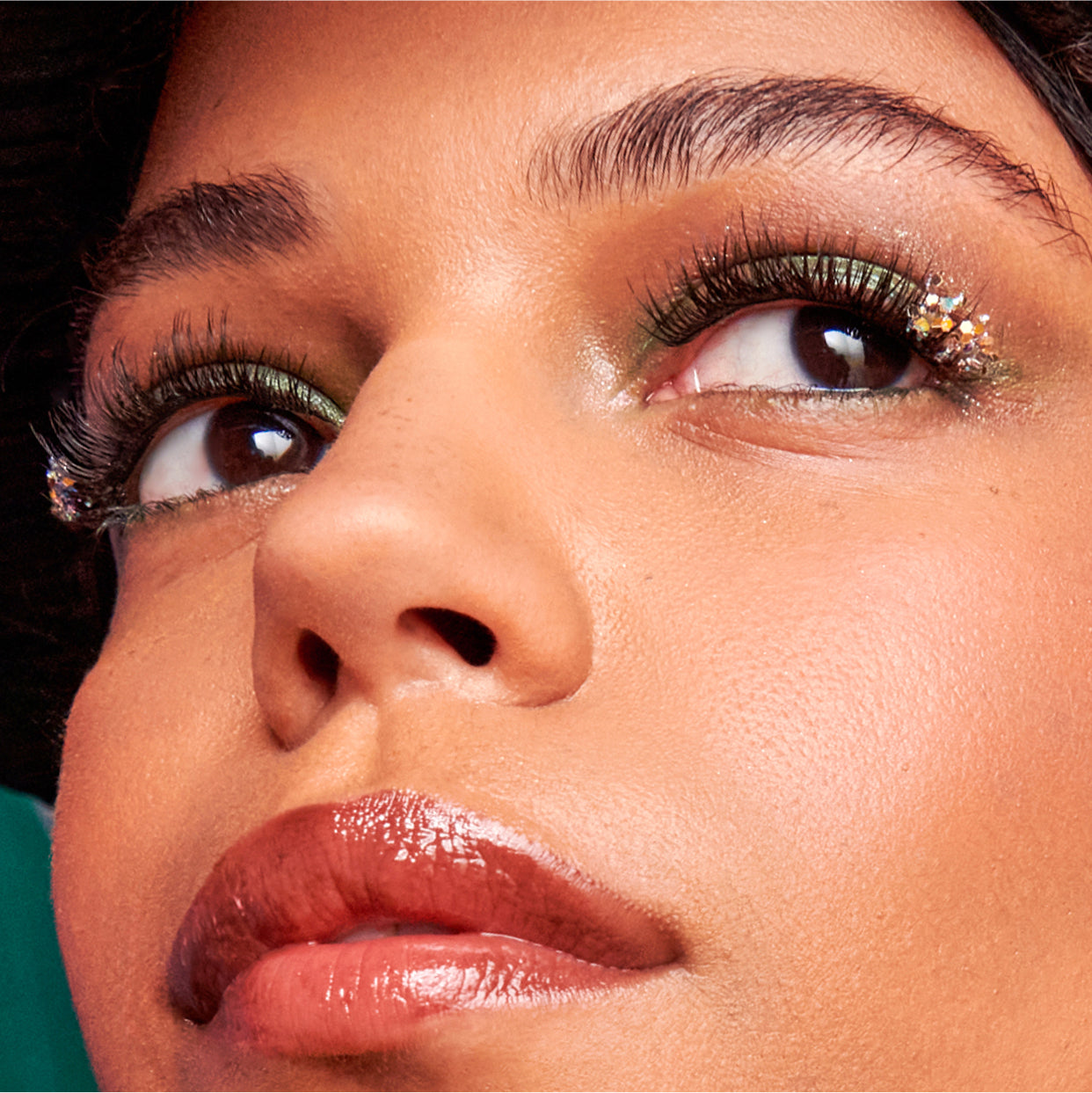 Close-up beauty shot showcasing glittery eyeshadow, bold lashes, and glossy lips.