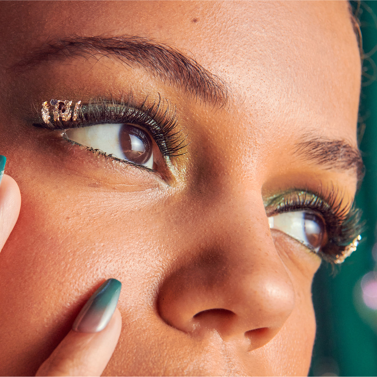 Close-up of woman's face with gold eyeshadow, winged eyeliner, and green nail polish