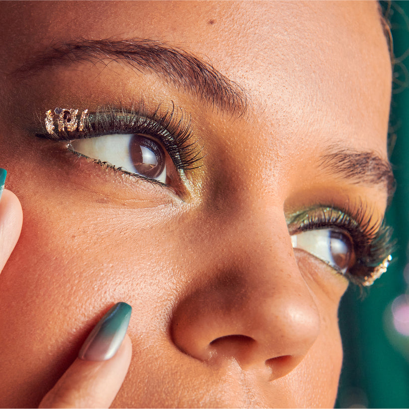 Close-up of woman's face with gold eyeshadow, winged eyeliner, and green nail polish