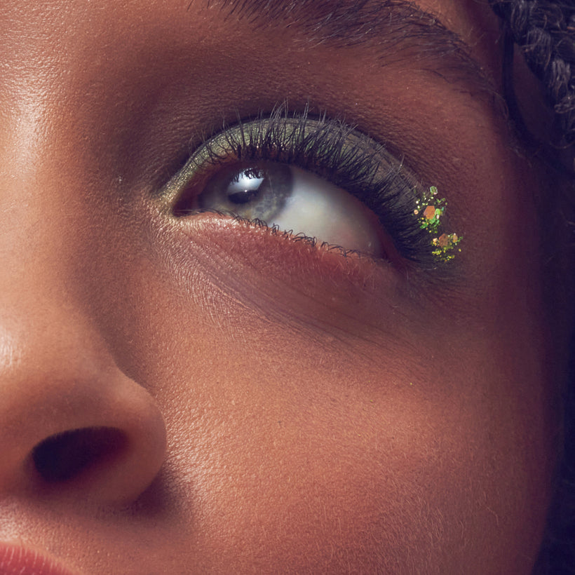 Close-up of eye makeup featuring gold eyeshadow, black winged eyeliner, and colorful glitter accent.