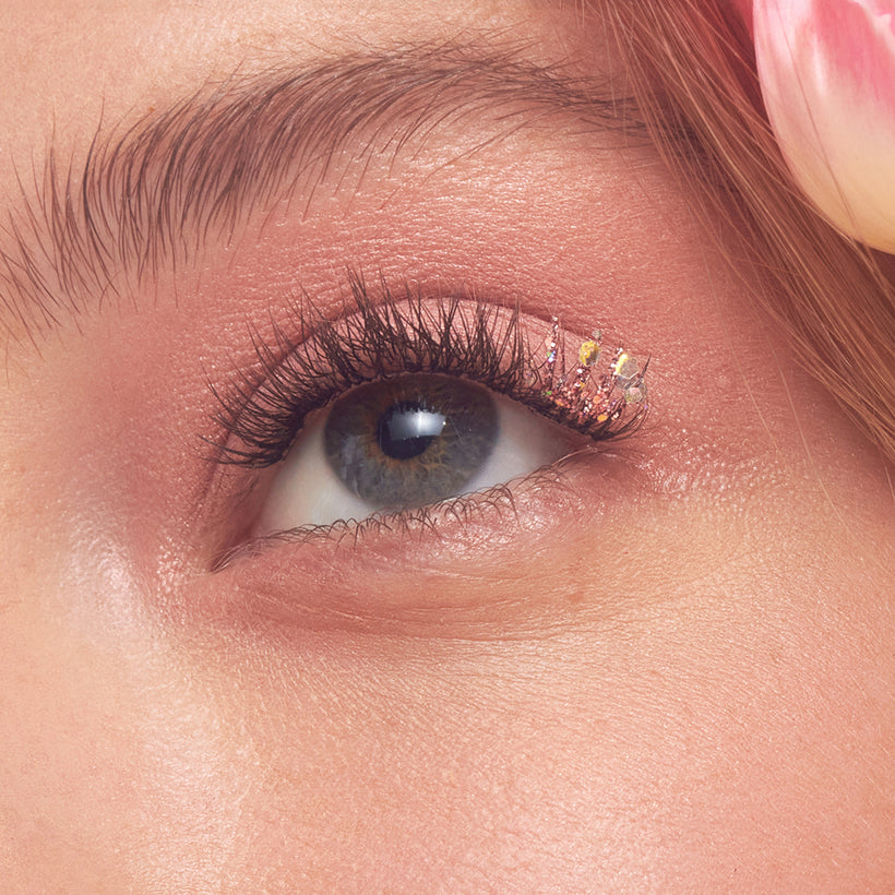 Close-up of eye with gold glitter eyeshadow and black mascara on warm-toned skin.