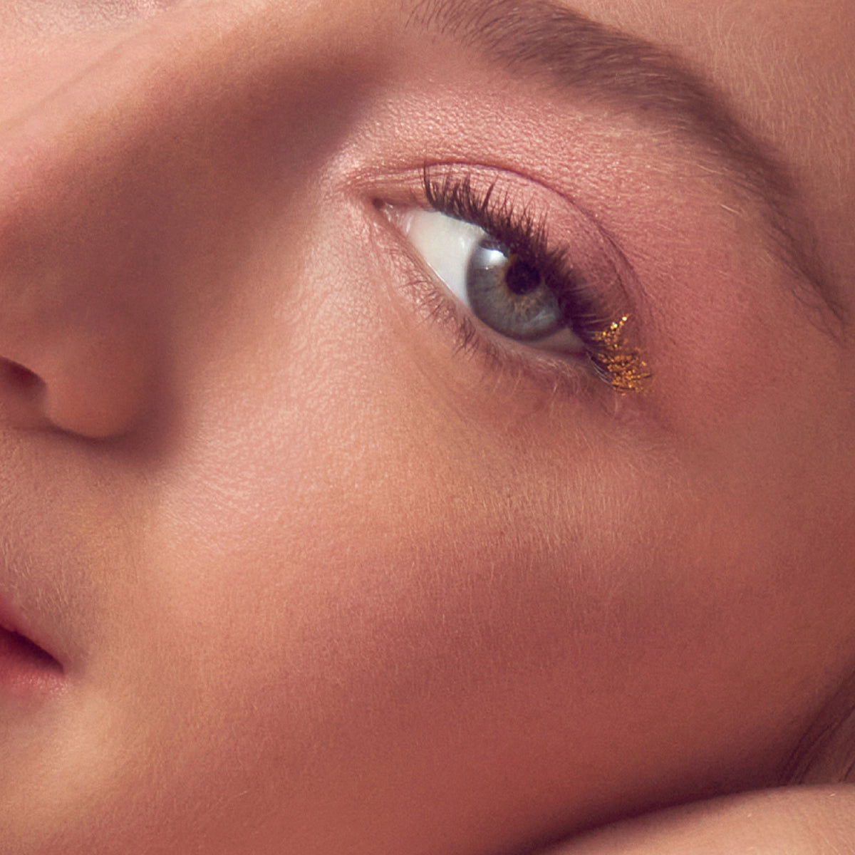 Close-up of eye makeup featuring burgundy eyeshadow and gold glitter accent on lower lash line.