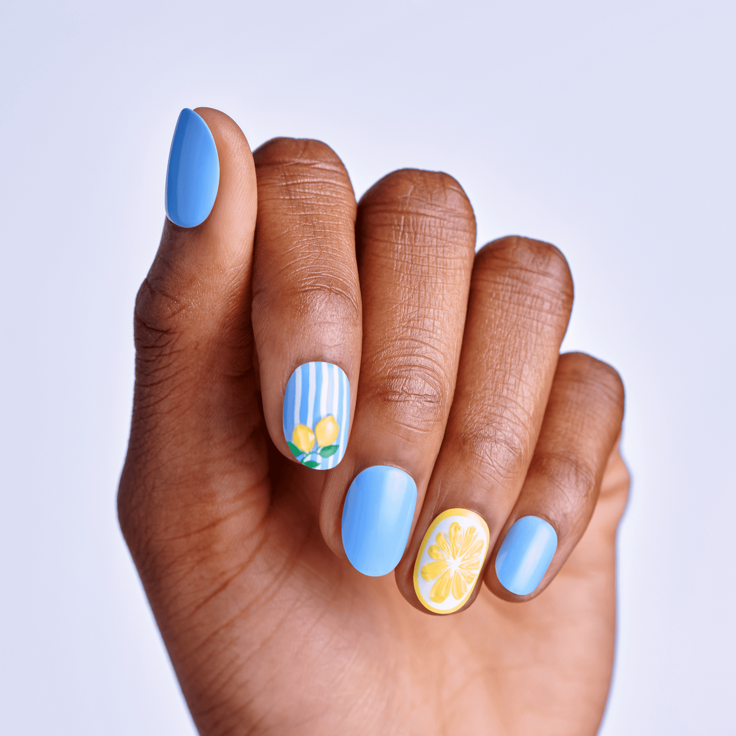 Hand with blue maniucre with stripes and lemon design on a light gray background