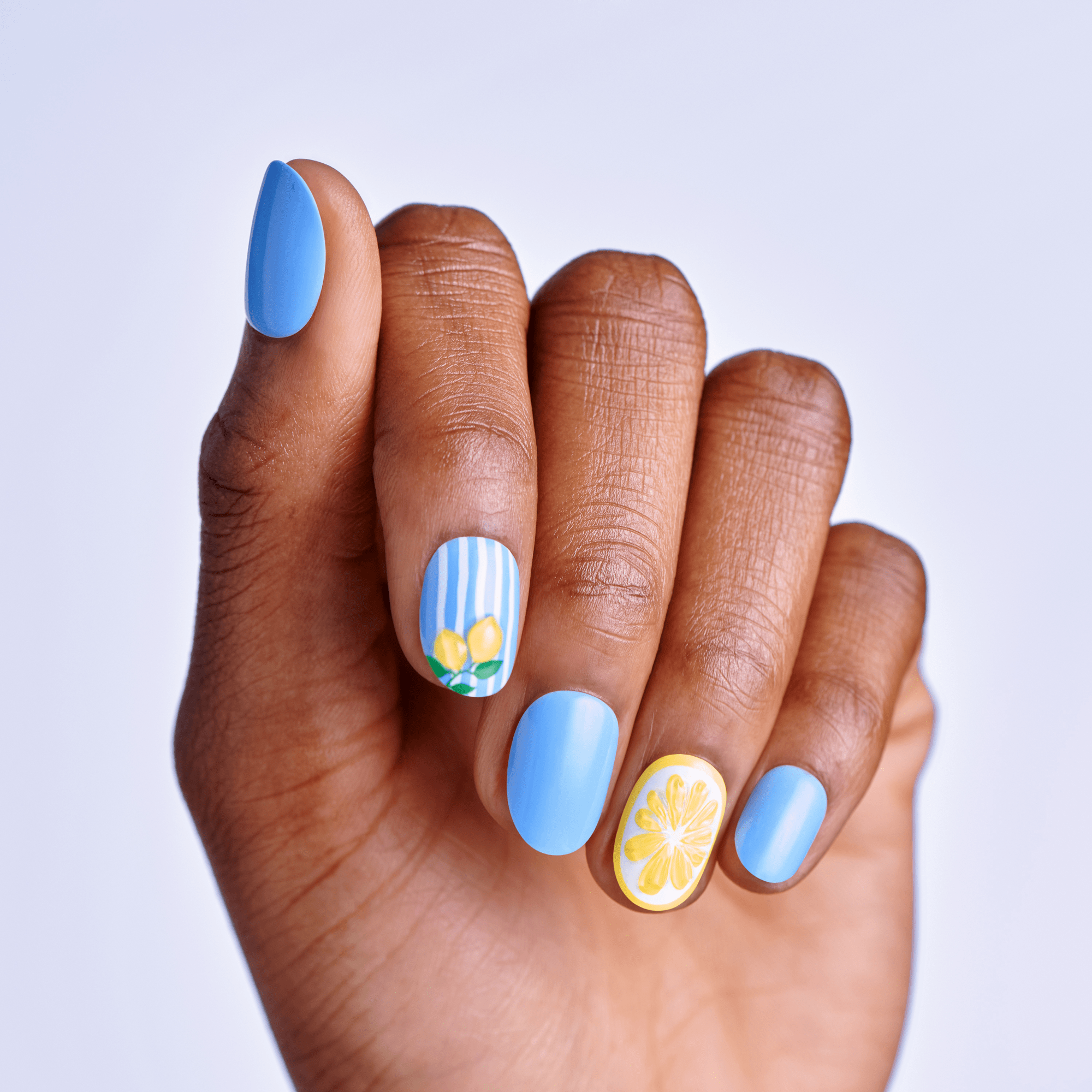 Hand with blue maniucre with stripes and lemon design on a light gray background