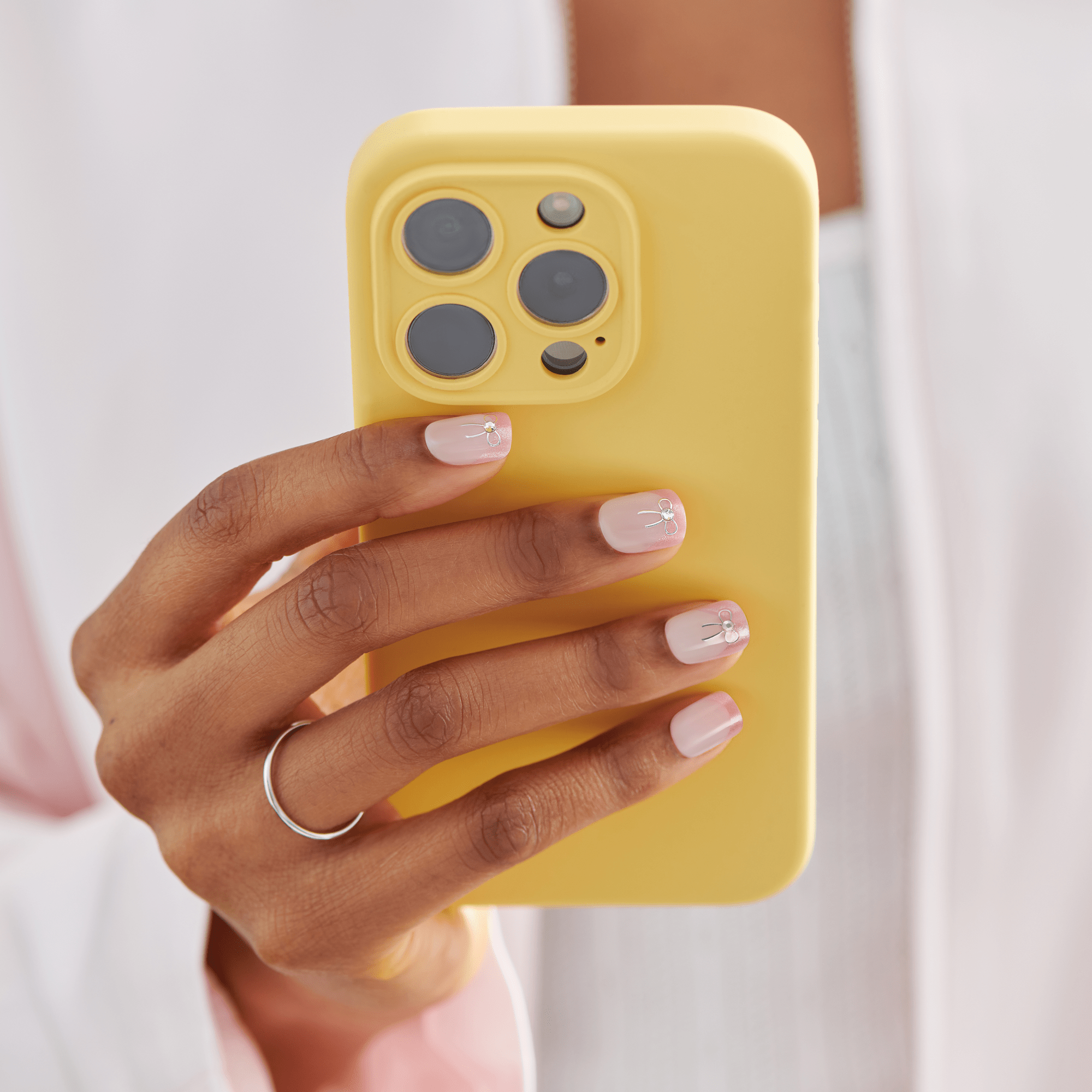 Yellow iPhone 14 Pro case held by hand with manicured nails and silver ring