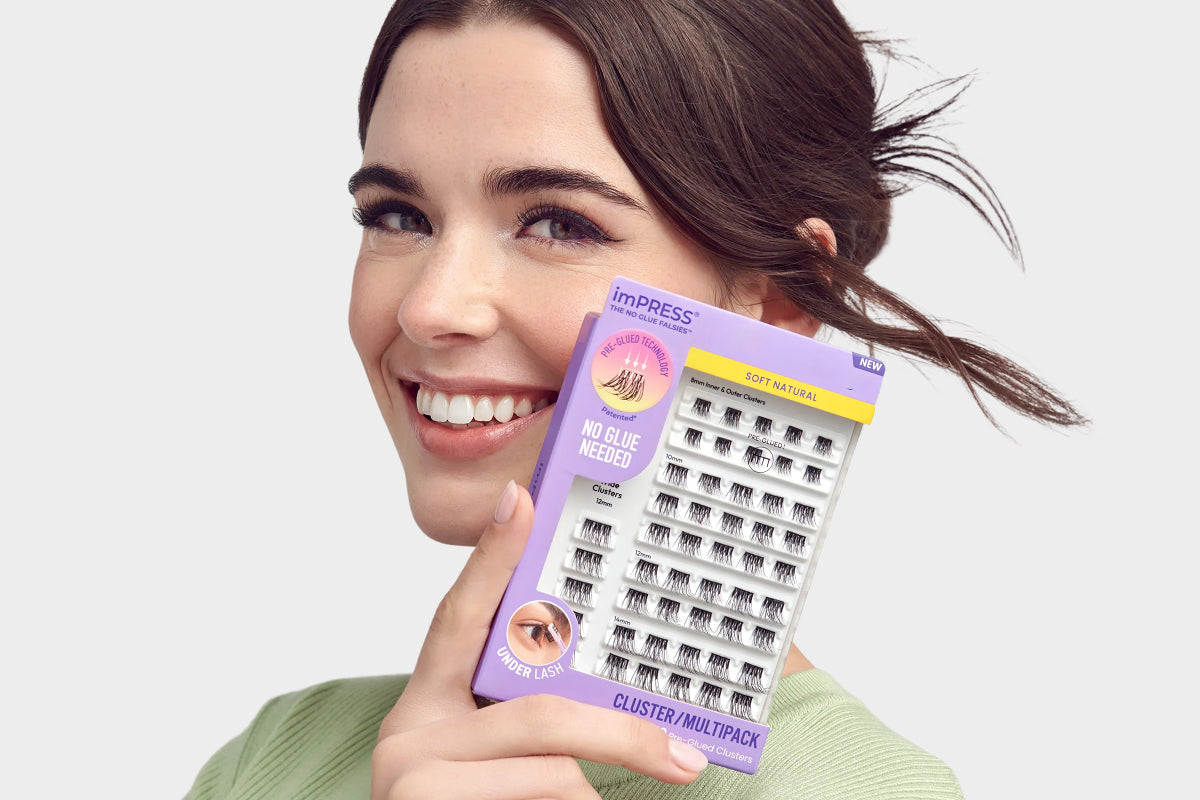 Woman holding imPRESS lash multipack box, smiling at camera against white background.