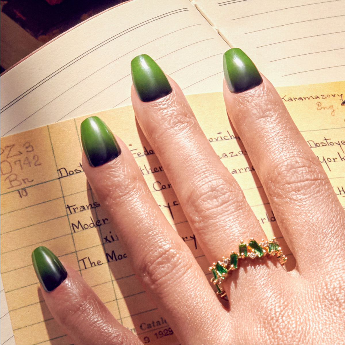 Green ombre almond nails with gold ring on open notebook pages