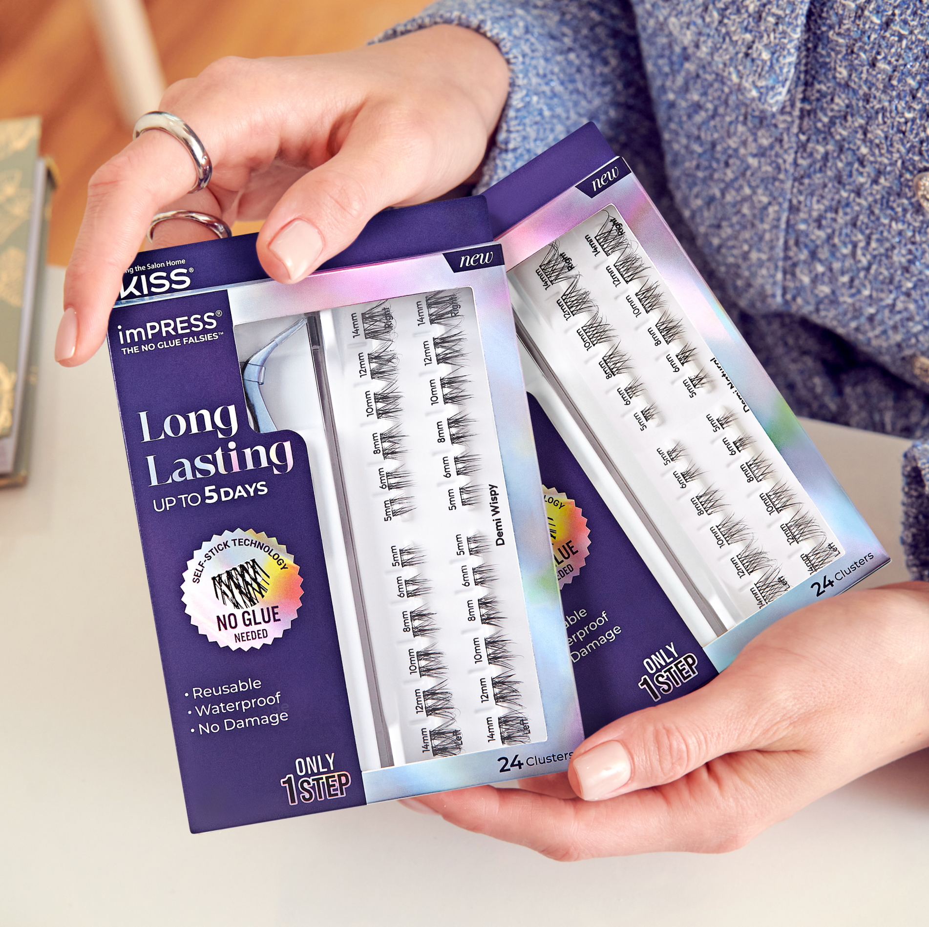 2 packages of imPRESS Long Lasting lash clusters being held in a person's hands. Packages indicate that lashes apply in 1 step and last up to 5 days. 