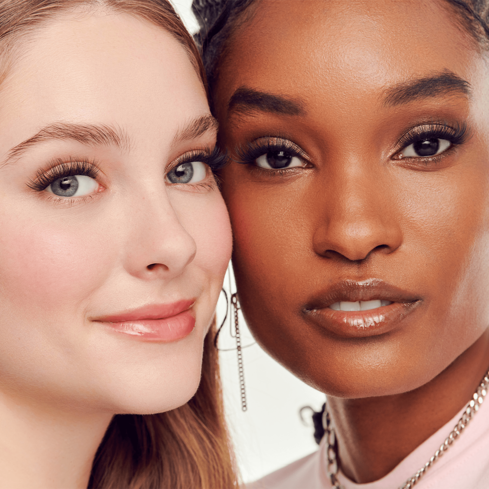Two women with close-up faces, one with blonde hair and blue eyes, the other with dark skin and brown eyes, against a neutral background.