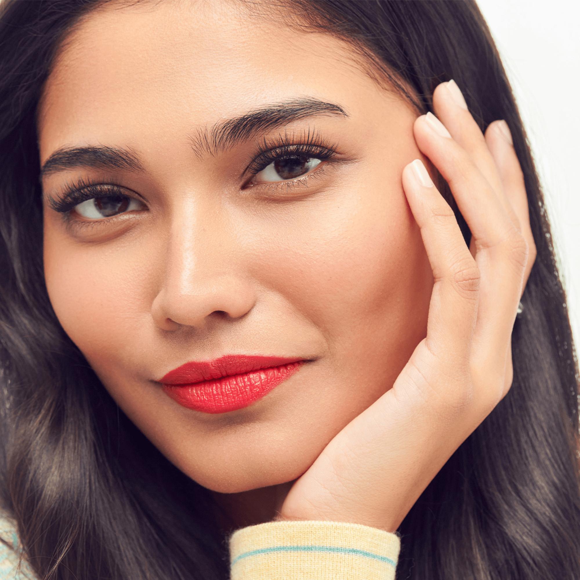 Close-up of a woman with red lipstick and hand on face against a neutral background